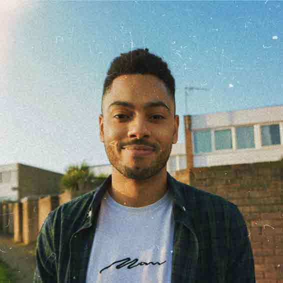Cameron headshot wearing white tshirt and flannel overshirt taken outside with blue sky in the background