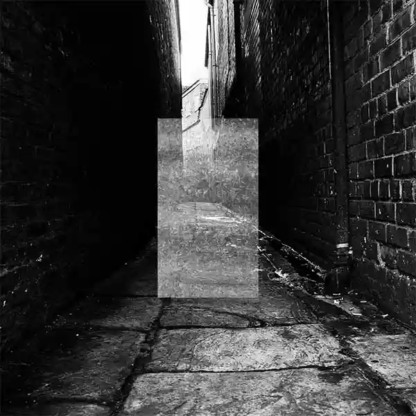 black and white photo of a dark paved alley ways between brick walls with a light grey transparent vertical rectangle in the centre